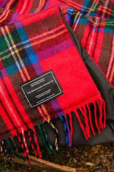 a red and green plaid blanket laying on the ground next to a black bag with a tag