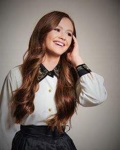 a woman with long brown hair wearing a white shirt and black skirt smiling at the camera