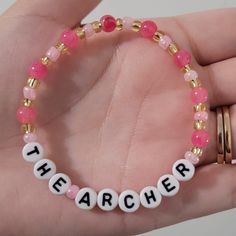 a hand holding a beaded bracelet with the word teacher spelled in white and pink beads