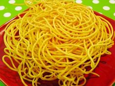 a red plate topped with yellow noodles on top of a green and white polka dot table cloth