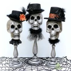 three skeleton heads wearing hats and feathers on top of a lace doily with an orange flower in the middle