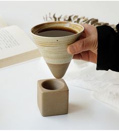 a person is holding a coffee cup in front of an open book on a table