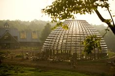 a large metal structure sitting in the middle of a lush green field next to a forest