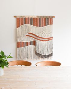 a wall hanging on the side of a white wall next to a potted plant