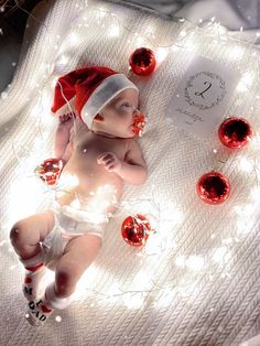 a baby wearing a santa hat and diaper laying on a blanket with christmas decorations around it