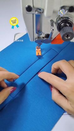 two hands working on a sewing machine with blue material in the foreground and an orange object in the background