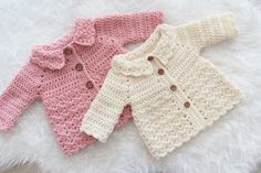 two crocheted sweaters laying on top of a white furnishing