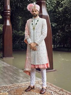 a man standing on top of a rug wearing a white suit and pink turban