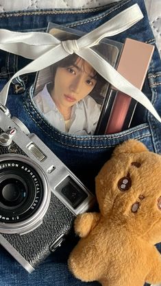 a teddy bear sitting next to a camera and some photos in the back pocket of someone's jeans