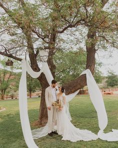 a bride and groom standing in front of a tree with white draping on it