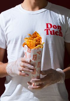 a man in white shirt holding up a paper container filled with fries