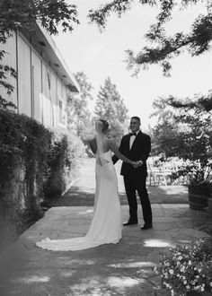 a bride and groom holding hands in front of a building with trees on the side