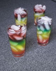 three glasses filled with different colored drinks on top of a gray floor next to each other