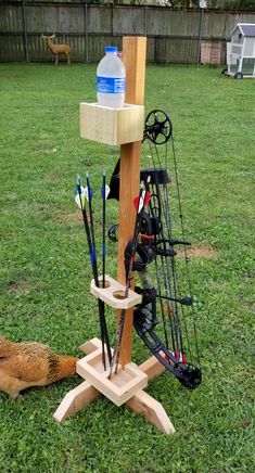 an outdoor archery stand with arrows, bows and water bottle on it in the grass