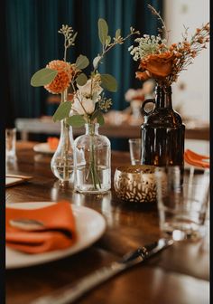 the table is set with orange napkins and flowers in glass vases on it