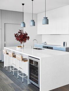 a kitchen with white counter tops and blue pendant lights hanging from the ceiling above it