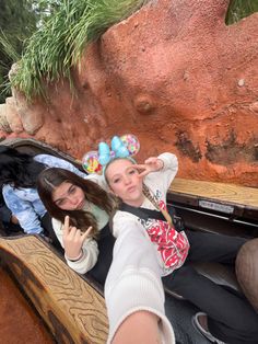 two young women sitting on a bench in front of a rock formation at the zoo