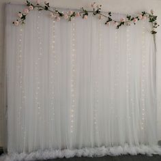 a white backdrop with flowers and lights on the top is decorated for a wedding or special event