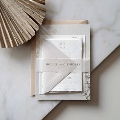 the wedding stationery is laid out on a marble table with a fan and seashell