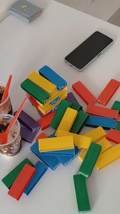 there are many pieces of colored paper on the table next to a cell phone and cup