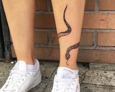 a woman's foot with a snake tattoo on her left leg and white tennis shoes