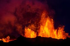 the lava is spewing up into the air at night time, with bright orange and red colors