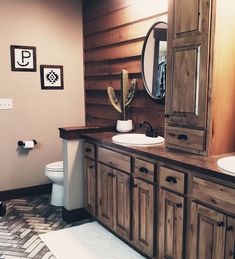 a bathroom with two sinks, a toilet and a wooden cabinet next to a mirror