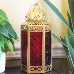 a red and gold lantern sitting on top of a table next to a potted plant