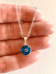 "Darling petite translucent London Blue evil eye charm on delicate sterling necklace. Handmade in Turkey this darling little two-sided translucent glass evil eye is only 3/8\" with sterling silver rim and bail. The beautiful London Blue color makes it even more striking. Petite charm hangs from delicate .925 sterling silver cable chain with spring ring clasp. Total drop with bail is 5/8\"." Adjustable Blue Sterling Silver Charm Necklace, Adjustable Sterling Silver Evil Eye Necklace, Handmade Blue Sterling Silver Charm Necklace, Sterling Silver Evil Eye Charm Necklace, Sterling Silver Evil Eye Necklace For Everyday, Blue Round Charm Necklaces For Everyday, Everyday Handmade Blue Charm Necklaces, Everyday Blue Charm Necklaces, Everyday Blue Round Charm Necklaces