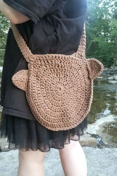 a woman is holding a crocheted bag in her hands and standing by the water