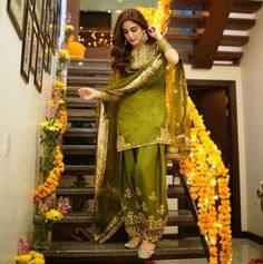 a woman standing on some stairs wearing a green outfit with gold trimmings and flowers