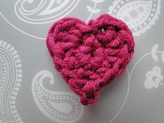 a pink crocheted heart sitting on top of a gray wallpaper covered with paisley