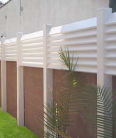 a row of white wooden slats next to a brick wall with grass growing on it