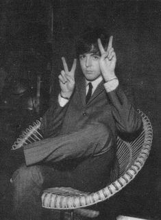 a young man sitting in a chair making the peace sign with his hands while wearing a suit and tie