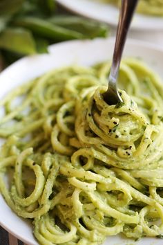 a fork is stuck into some green pasta on a plate with another dish in the background