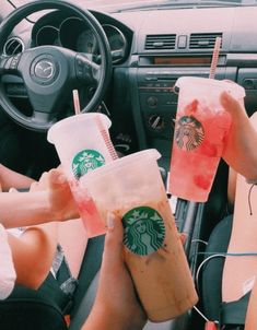 two people holding drinks in their hands while sitting in the drivers seat of a car