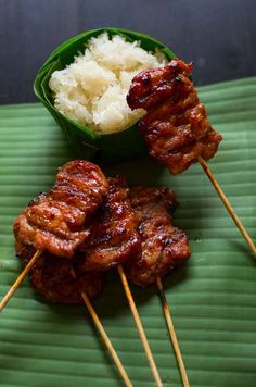 several skewers of meat and rice on a green plate