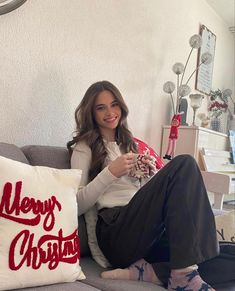 a woman sitting on a couch holding a christmas pillow