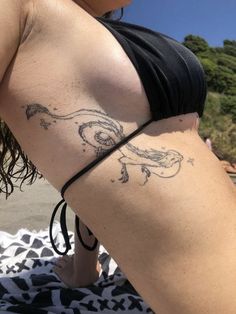 a woman with a tattoo on her back is sitting on the beach and looking at the water