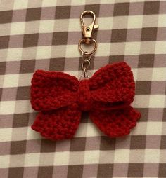 a red knitted bow keychain on a checkered tablecloth with a metal hook