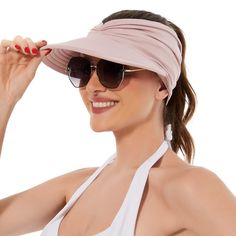 a woman wearing sunglasses and a pink visor smiles at the camera while holding her hair in one hand