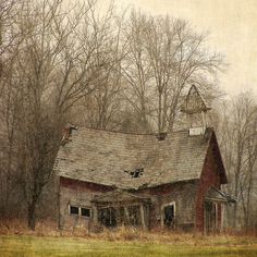 an old red barn in the middle of a field with trees and grass around it