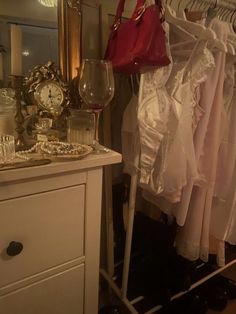 there is a rack with dresses and wine glasses next to the dresser in this room