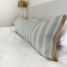 a close up of a pillow on a bed with white linens and striped pillows