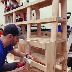 a man in a blue shirt and black hat working on some wooden shelves with tools