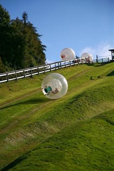 three large balls floating in the air on top of a grass covered hill next to a wooden fence