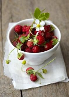 strawberries in a white bowl on a napkin with green leaves and flowers around it