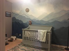 a baby's room with mountains painted on the wall and a crib in the foreground