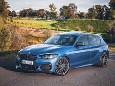 a blue bmw is parked on the side of the road in front of some bushes