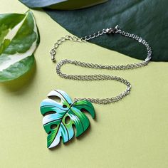 "Inspired by the Albo Borsigiana variegated monstera deliciosa, this unique heart-shaped leaf necklace will add a luxurious botanical flair to your wardrobe or bring a personal hand-made touch as a gift to a loved one. This original design is hand painted on cherry wood with a beautiful patchwork palette of white and green. The subtle heart shape of the leaf adds even more character to an already unique necklace. Lightweight and durable, this necklace is sure to capture the heart of any plant lo Multicolor Leaf-shaped Jewelry Gift, Multicolor Leaf Shaped Jewelry For Gifts, Trendy Leaf-shaped Jewelry Gift, Trendy Green Leaf-shaped Jewelry, Handmade Tropical Green Jewelry, Handmade Multicolor Leaf-shaped Jewelry, Green Leaf-shaped Botanical Jewelry, Tropical Style Multicolor Jewelry As Gift, Handmade Green Leaf Necklace